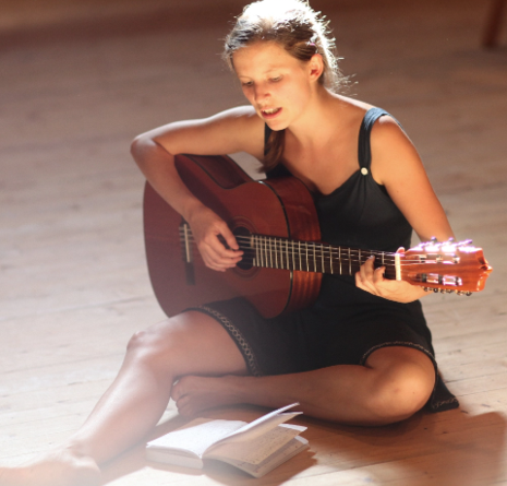 Eine Frau sitzt auf dem Boden, singt und spielt Gitarre
