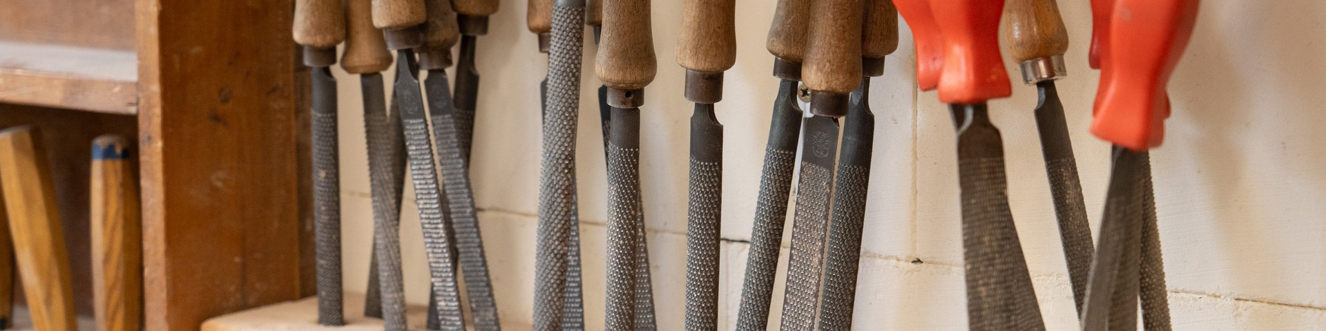 Eine Reihe von Holzraspeln mit Griffen ist in einem hölzernen Halter in einer Werkstatt vor einer weißen Wand ordentlich angeordnet.
