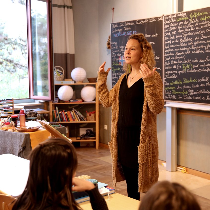 Eine Lehrerin steht vor den Schülern und erklärt etwas