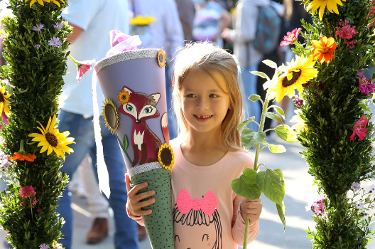 Fröhliches Kind mit einer Schultüte und Blume in der Hand